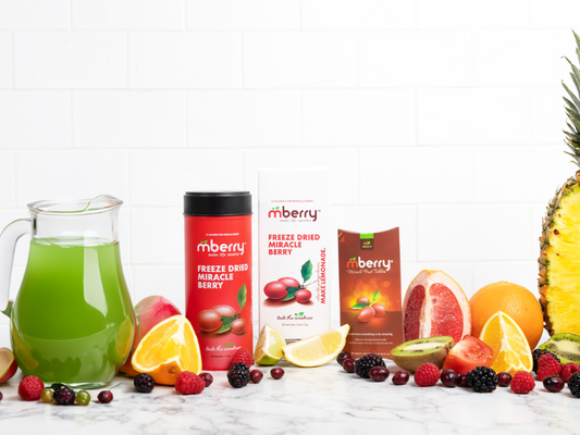 mberry hero image with green juice, freeze dried miracle berries, miracle fruit tablets with fruit like lemons, limes, pineapple, kiwi, grapefruit, blackberries, raspberries, and rhubarb